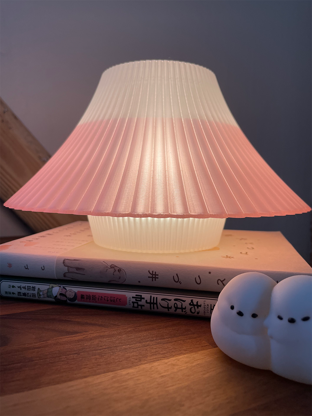Glowing pink and white 3D printed Fuji desk lamp on a stack of books on a wooden desk